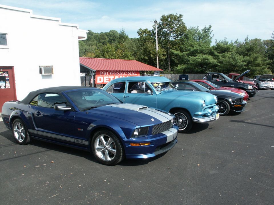 Blue convertible Mustang with silver racing stripes parked in a line of cars
