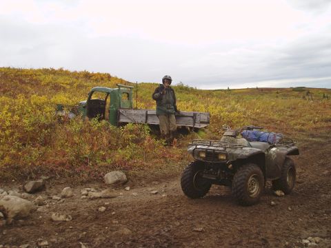 2000 Ford E350 - An old green flatbed truck sits abandoned in a field next to a parked ATV.