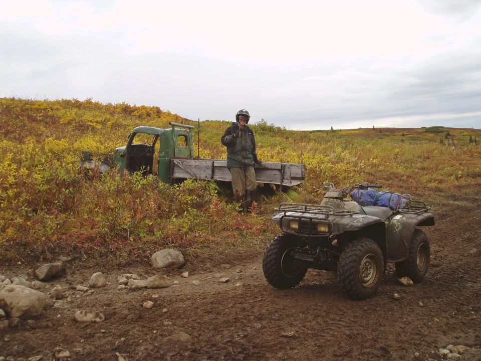 Green flatbed truck and ATV in a field with autumn foliage