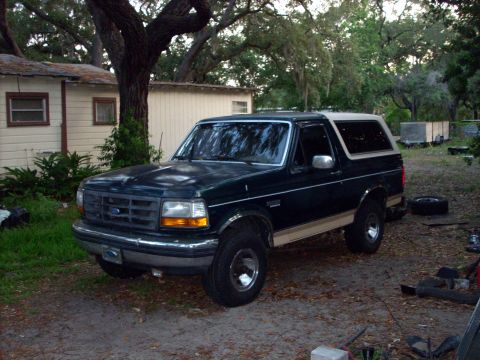 1992 Ford Bronco - A dark green 1992 Ford Bronco with tan trim is parked in a yard next to a house.