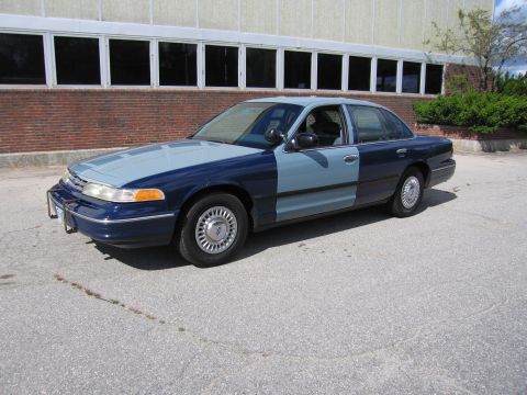 2001 Ford Crown Victoria - A two-tone Ford Crown Victoria is parked in front of a brick and glass building.
