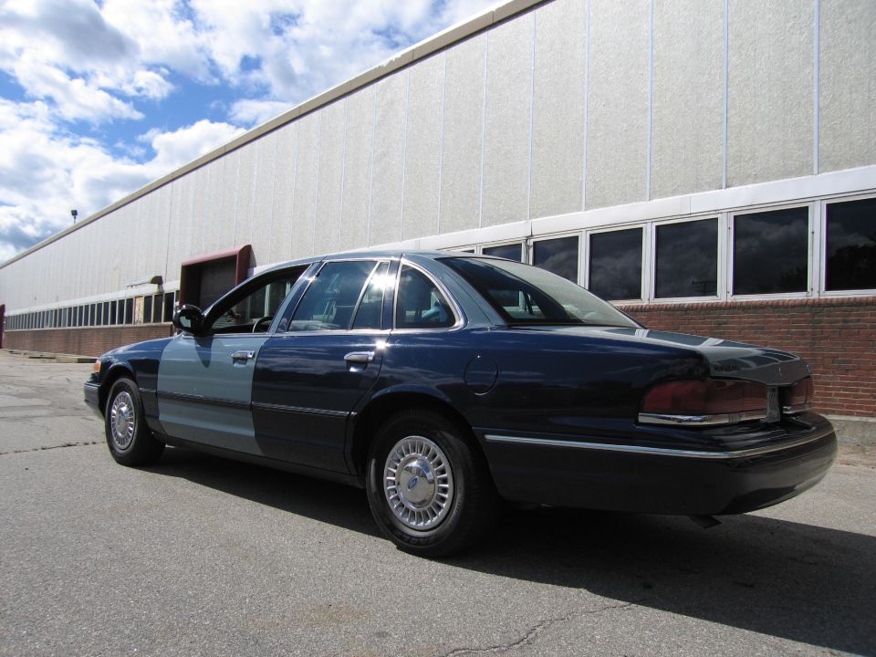 Two-tone blue Ford Crown Victoria sedan, rear three-quarter view by warehouse