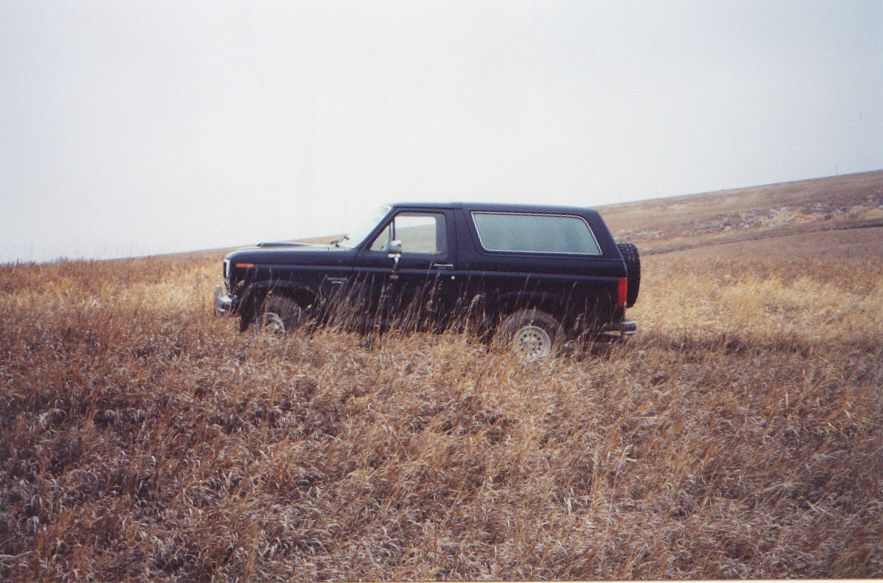 Dark Ford Bronco in profile parked in tall dry grass on open prairie hills