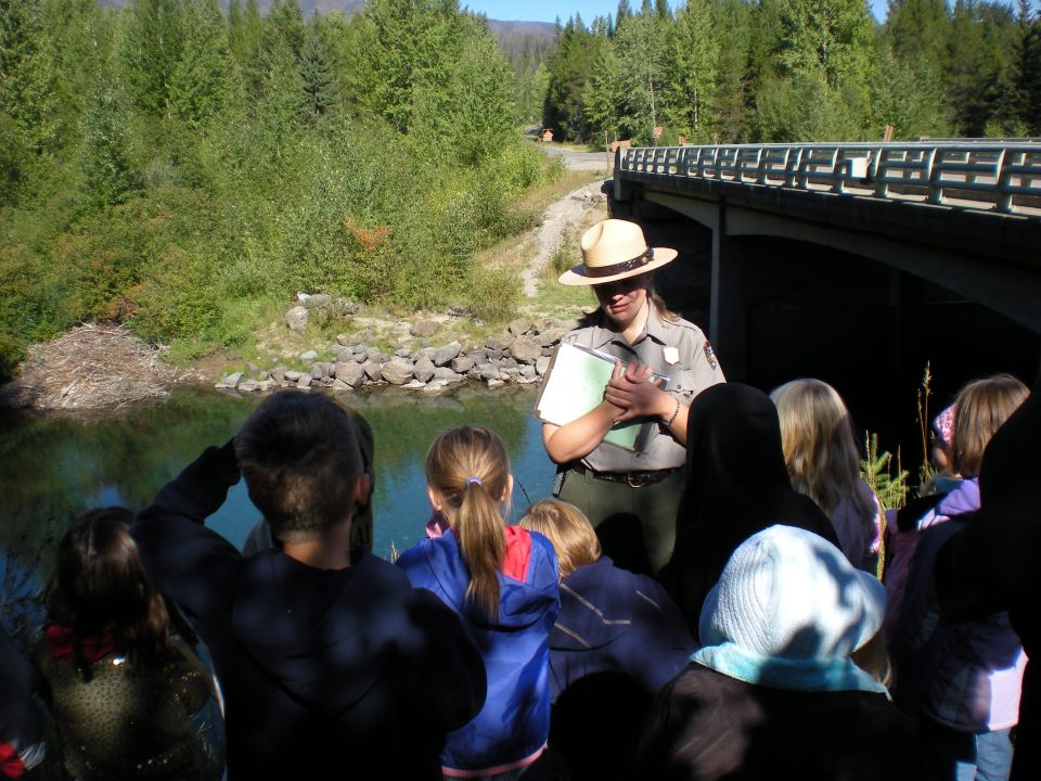Park ranger giving a presentation to a group of people by a bridge and water.
