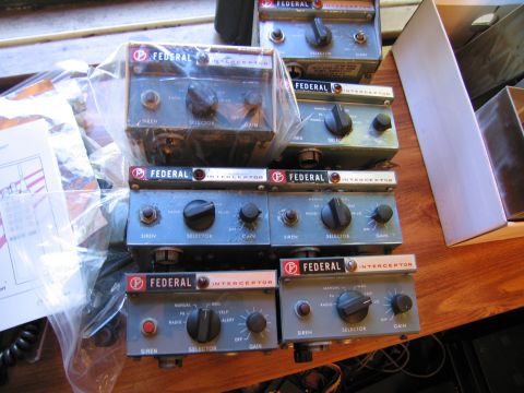 1991 Ford LTD Crown Victoria - collection of vintage gray Federal Interceptor siren control heads with selector and gain knobs sits grouped on a wooden workbench.