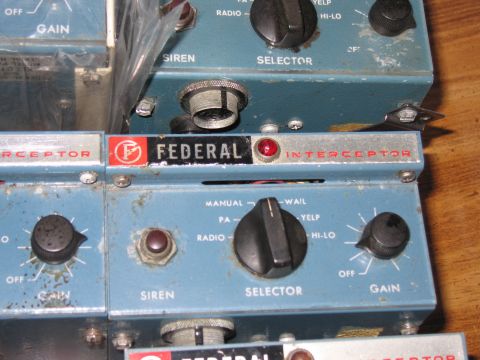1991 Ford LTD Crown Victoria - Worn blue Federal Interceptor siren control heads with chipped paint sit stacked together on a wooden surface.