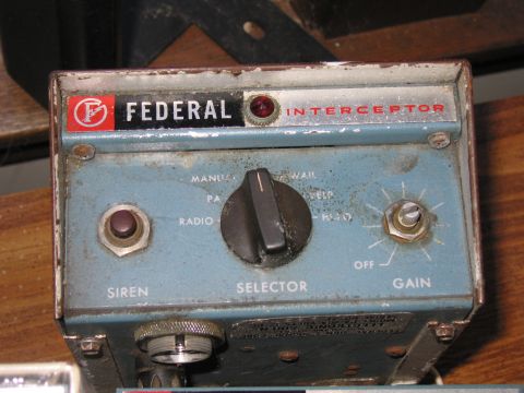 1991 Ford LTD Crown Victoria - single weathered blue Federal Interceptor siren control head with a chrome bezel and toggle selector stands on a wooden bench.