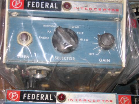 1991 Ford LTD Crown Victoria - Blue Federal Interceptor siren control heads wrapped in clear plastic bags are stacked together for storage.