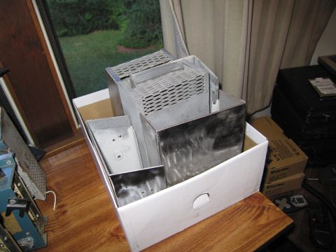 1991 Ford LTD Crown Victoria - Galvanized sheet-metal chassis enclosures with louvered vents fill a white cardboard box near a curtained window.