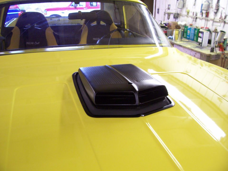 Black hood scoop on yellow hood of a car in a garage