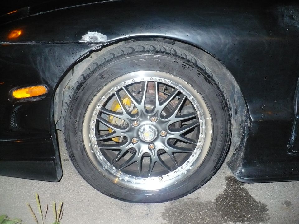 Black car front passenger wheel with silver multi-spoke aftermarket rim and yellow brake caliper.