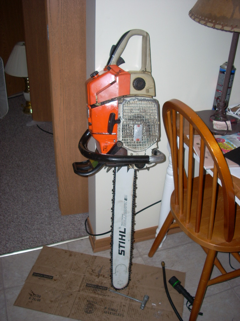 Stihl chainsaw standing upright on cardboard next to a wooden chair.