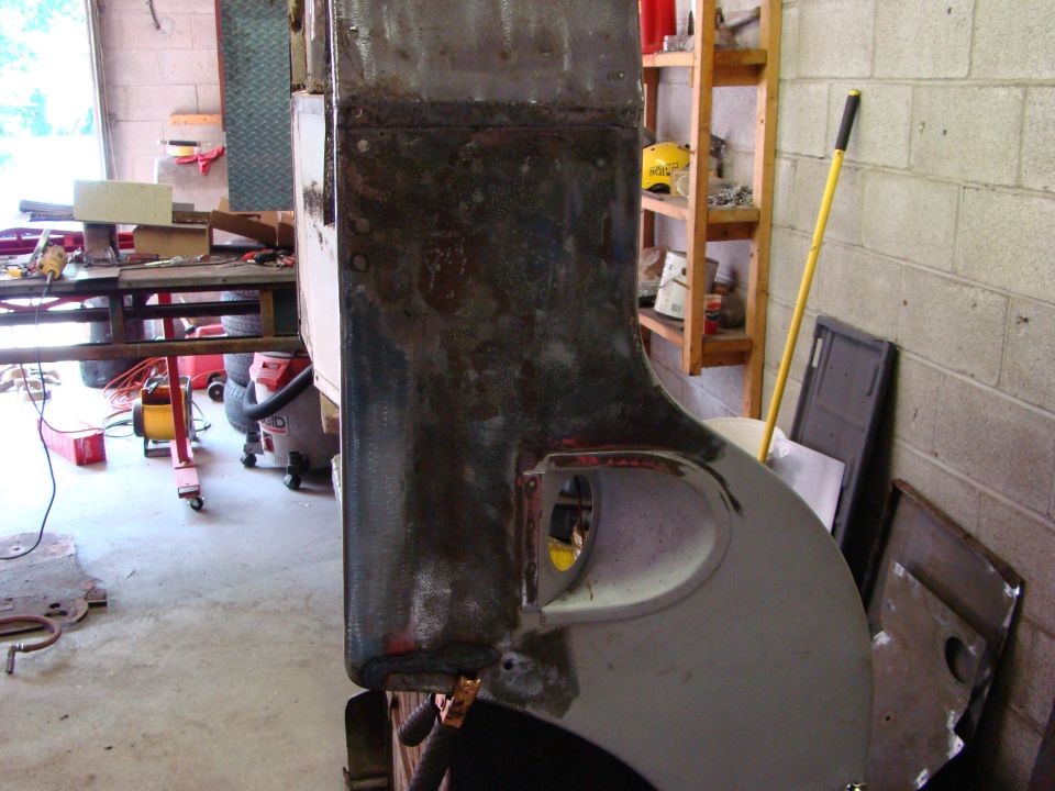 Rusted and primed vehicle body panel with a cutout, in a workshop setting.