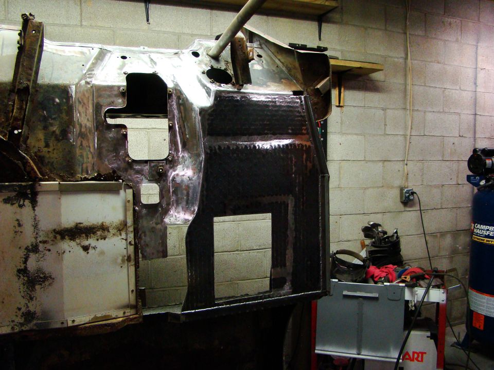 Jeep CJ chassis in workshop, undergoing restoration with exposed metal and dark coating.