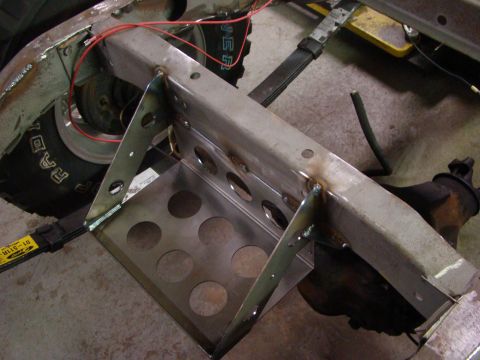 1948 Jeep Wrangler - A custom-fabricated metal battery tray with circular cutouts is welded to the frame of a vehicle, near the rear leaf spring and tire. Red e…