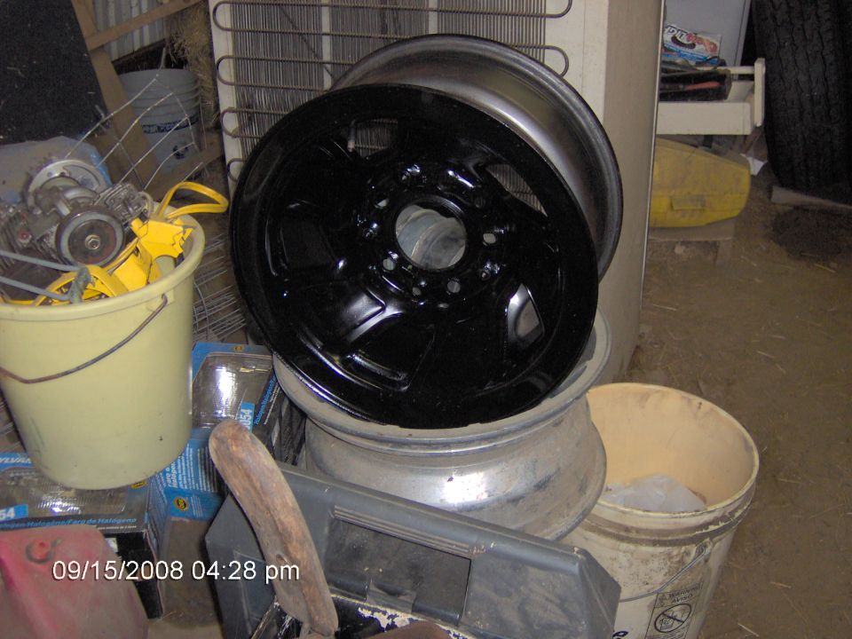 Black-painted steel wheel resting on a barrel in a cluttered garage