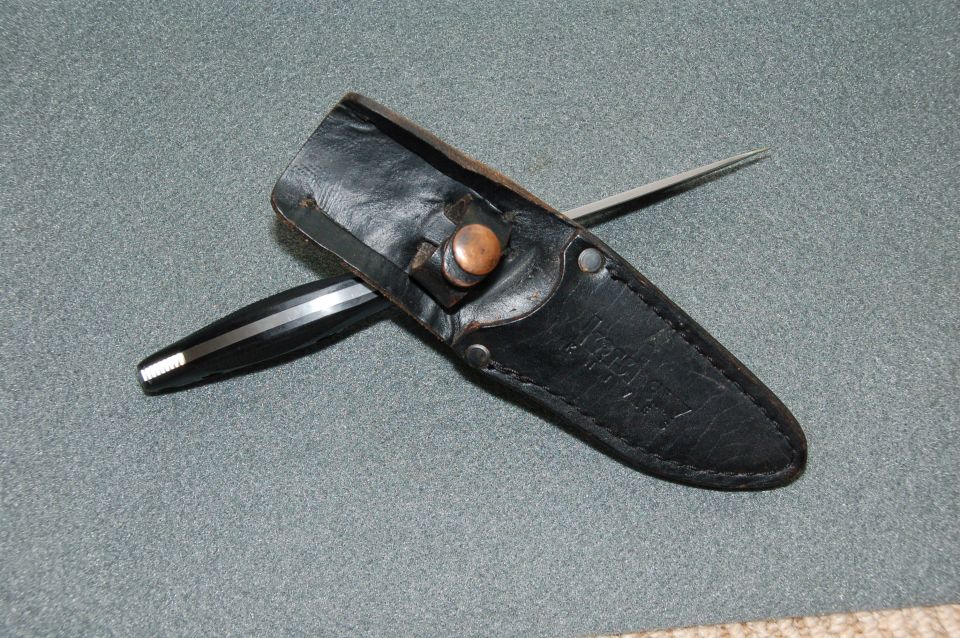 Black leather knife sheath with copper snap and partial knife visible
