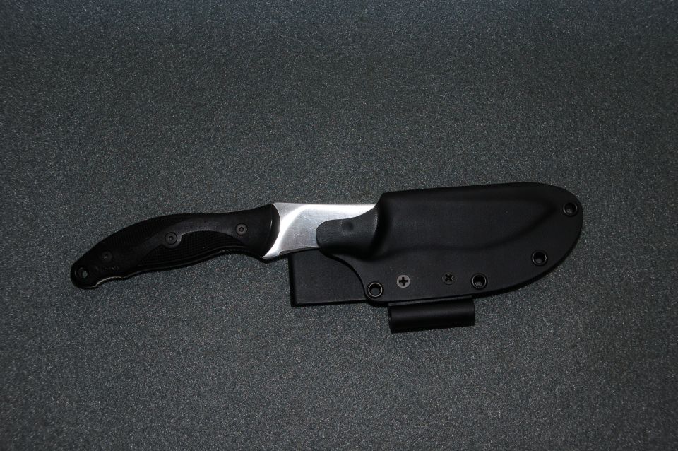 Fixed-blade knife sheathed in a black Kydex sheath on grey fabric