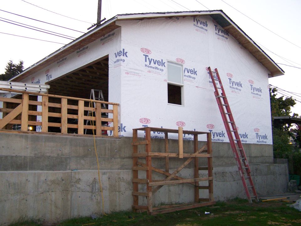 Tyvek-wrapped garage on a concrete foundation with ladders at dusk