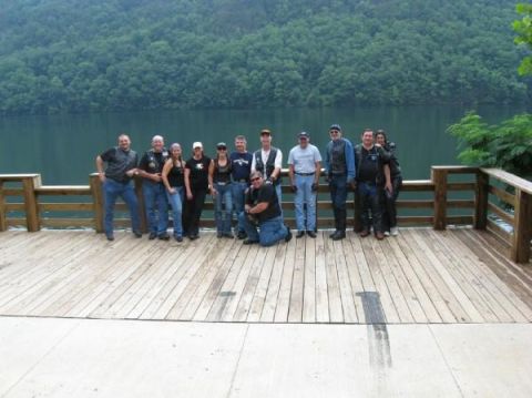 1996 Ford Crown Victoria - A group of people stand on a wooden deck overlooking a lake with a tree-covered mountain in the background.