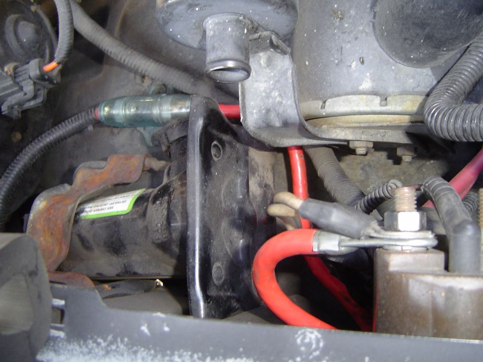 Engine bay close-up showing starter, red battery cable, and oxygen sensor