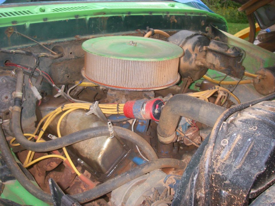 Engine bay of a green truck showing a round air cleaner on a carbureted V8