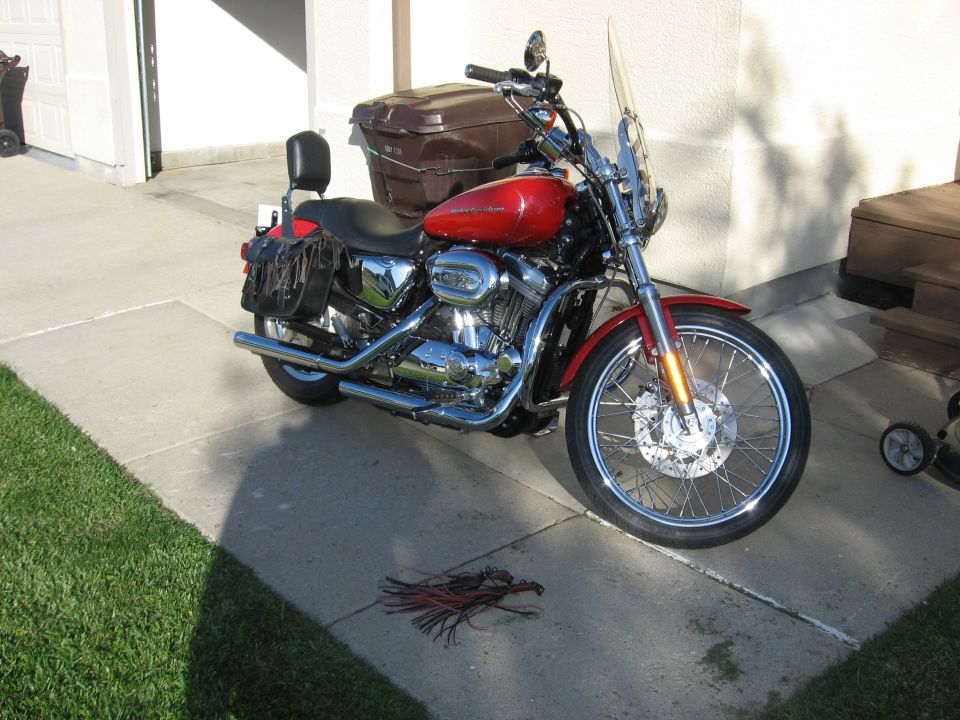 Red Harley-Davidson Sportster motorcycle with black saddlebags and windshield parked on a driveway.