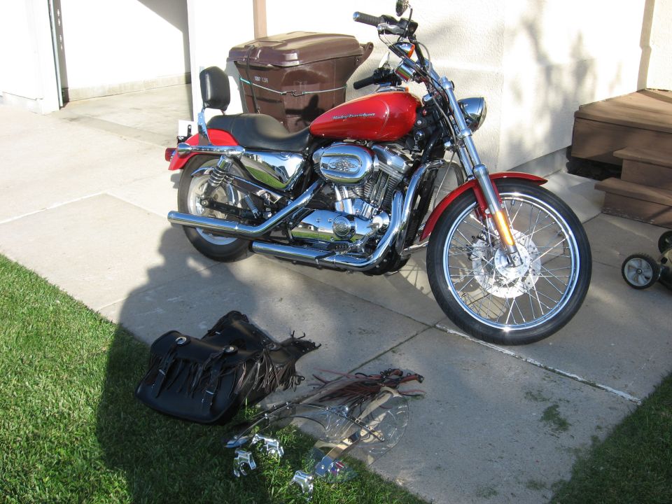 Red Harley-Davidson Sportster motorcycle parked on a driveway with saddlebag and windshield on the grass.
