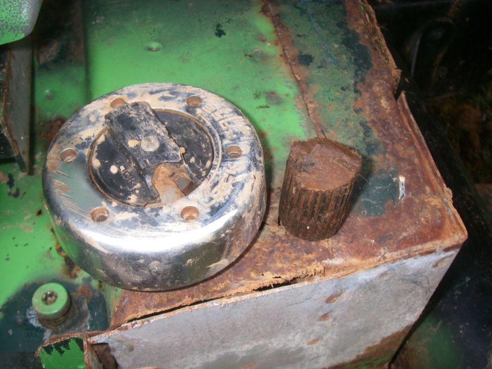 Close-up of a dirty, rusty chrome fuel cap on a rusted green surface next to a small rusty metal piece.