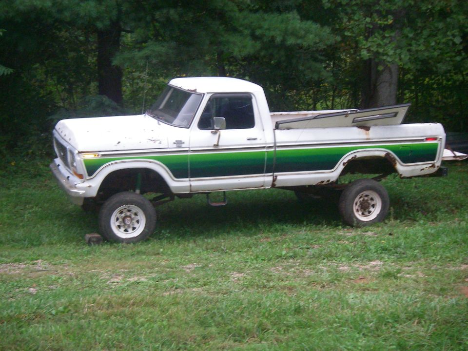 Lifted white and green Ford pickup truck with open camper shell lid, parked on grass.