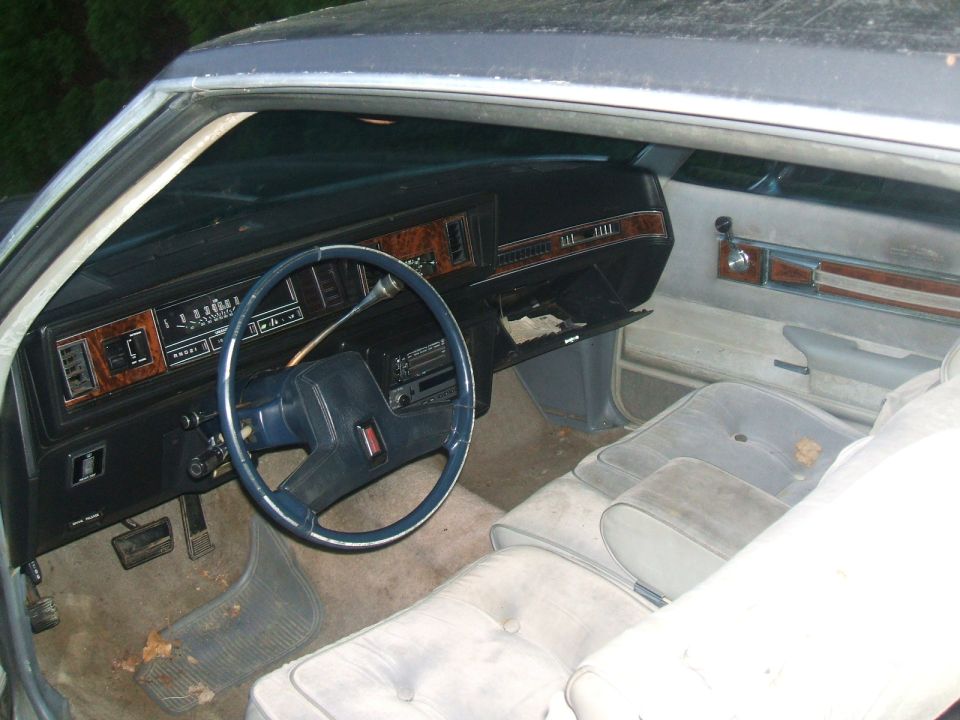 Faded blue dashboard, Oldsmobile steering wheel and gray bench seat in a 1980s coupe
