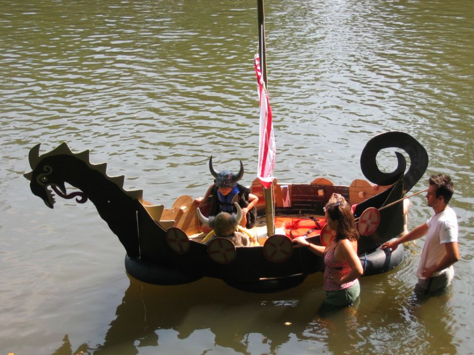 Homemade Viking dragon-head boat with people in horned helmets on a river