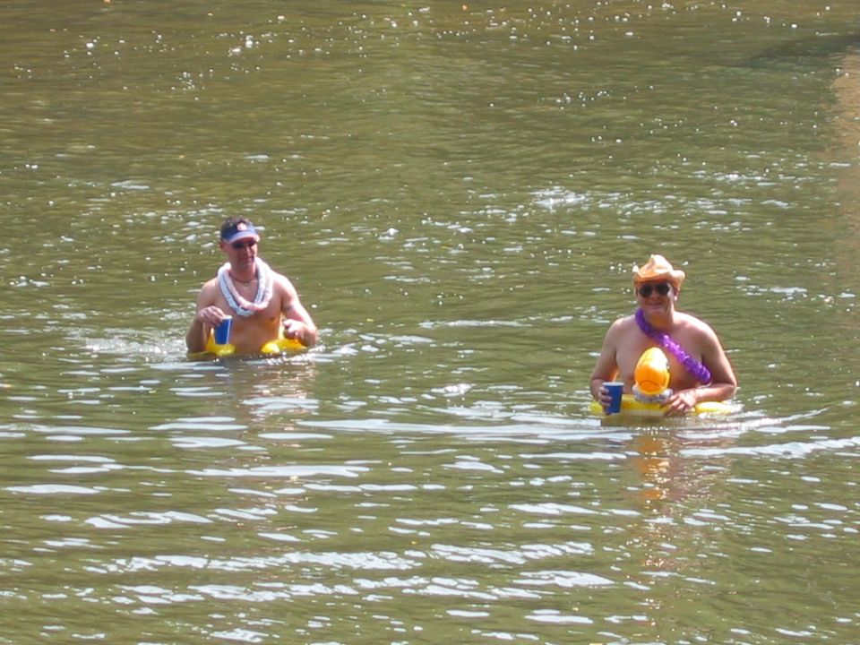 Two men floating in a river on yellow inner tubes wearing hats