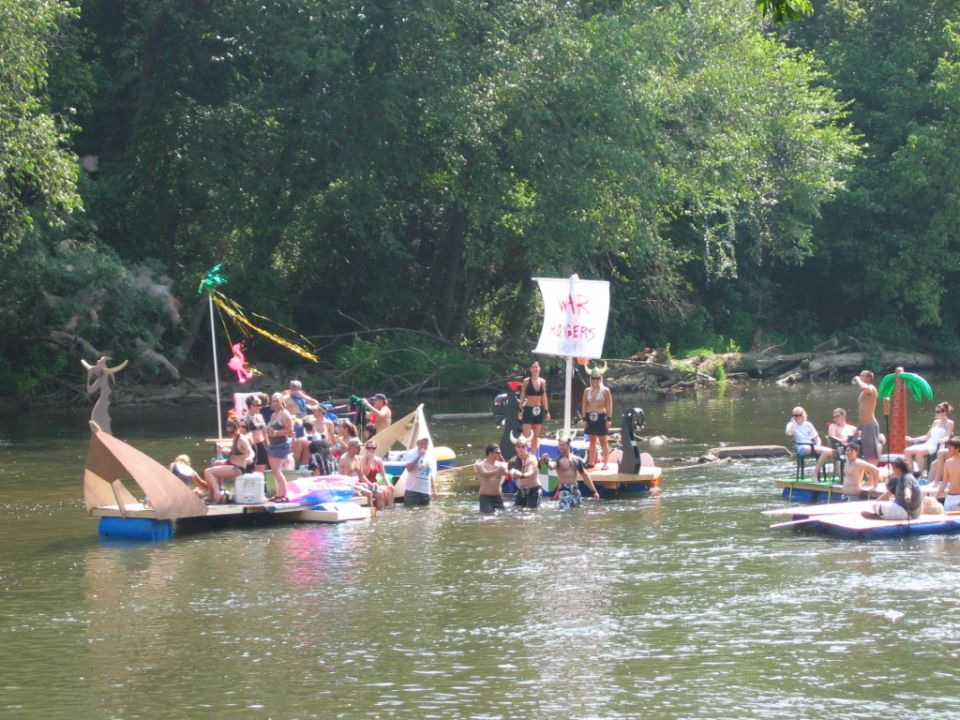 Several decorated rafts and people floating together on a river