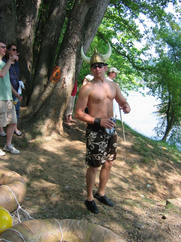 Man in a horned Viking helmet standing on a wooded riverside path