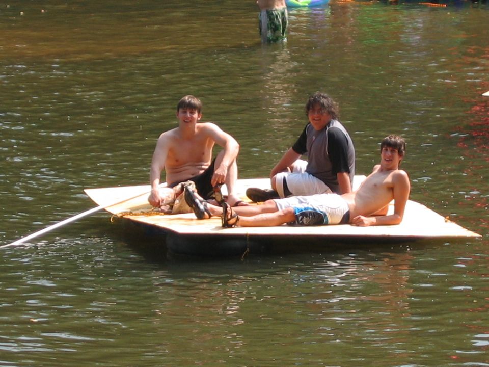Three young men relaxing on a small flat homemade raft on a river