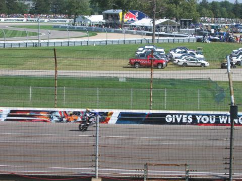 1985 Ford LTD Crown Victoria - Photograph of a motorcycle race with track support vehicles; not a technical document.