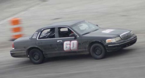2003 Ford Crown Victoria - A black Ford Crown Victoria race car with the number "60" in white with red trim is shown on a paved track, possibly during a race or pract…