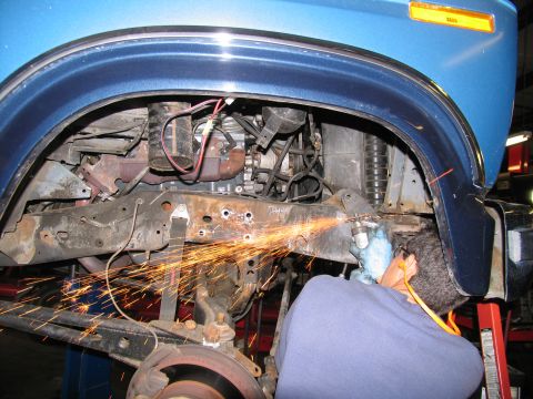 1984 Ford Bronco - A person wearing blue gloves and a blue sweatshirt uses a grinder to cut metal on the frame of a blue vehicle, with sparks flying. The vehi…