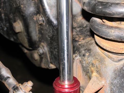 1984 Ford Bronco - A close-up view of a vehicle's suspension system shows a chrome shock absorber with a red base, positioned next to a rusty coil spring and…