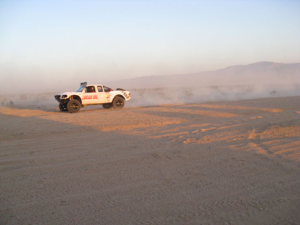 White off-road racing truck with Lucas Oil decals kicking up dust in a desert.