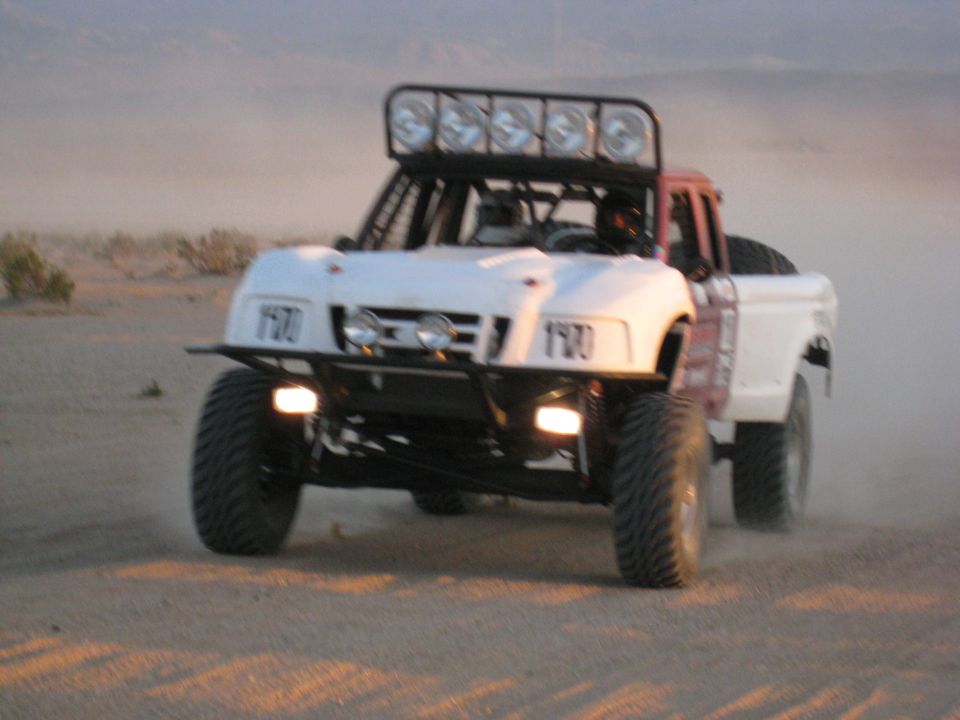 White and red off-road buggy with number 1970 driving on a dusty, sandy terrain.