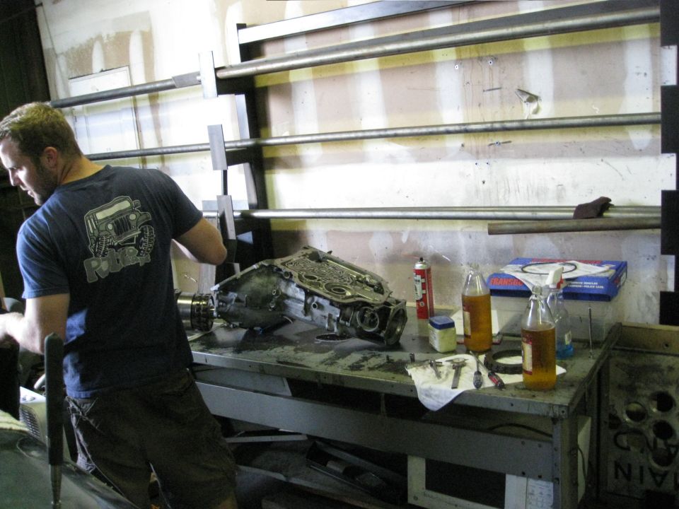 Man working on a disassembled Jeep transmission in a garage.