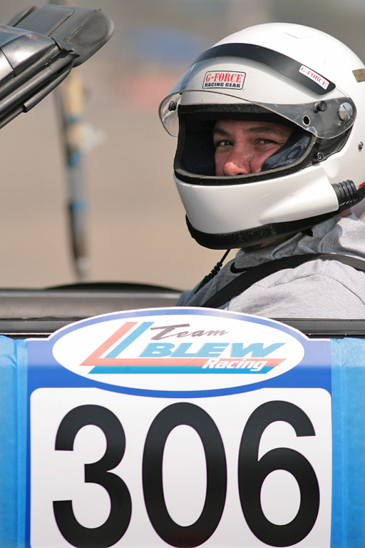Driver in white G-Force helmet in open-top race car with Team BLEW Racing 306 door number