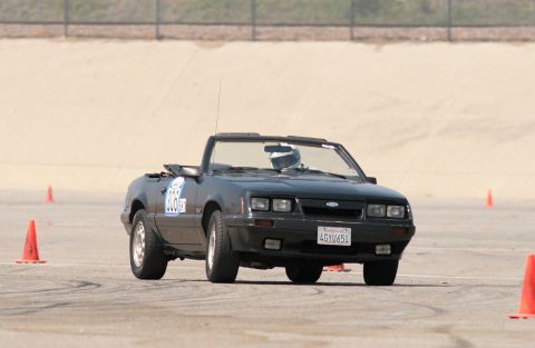 1985 Ford Mustang - Black Fox-body Ford Mustang GT convertible cornering hard on an autocross course with the top down, body rolled and the inside front wheel…