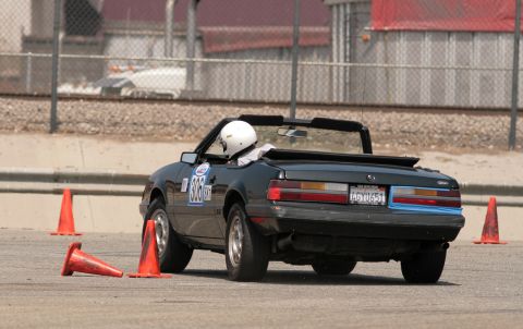 1985 Ford Mustang - Rear three-quarter view of a black Fox-body Mustang convertible running an autocross, top down with a roll bar and a driver in a white helm…