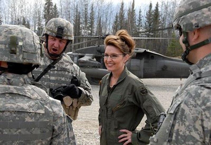 Woman in flight suit talking to soldiers in front of a helicopter