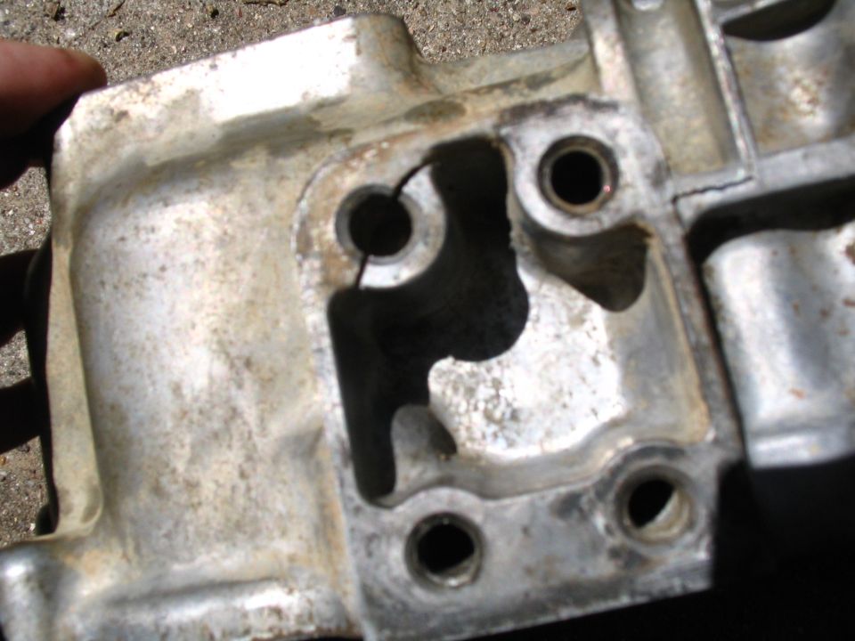 Damaged aluminum engine part with crack and holes on gravel