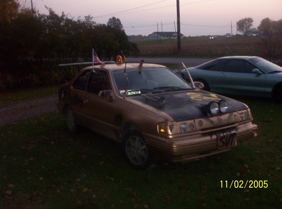 Gold sedan with black hood and extra lights, parked on grass.