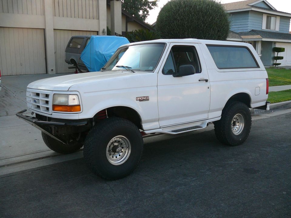 White 1988 Ford Bronco with custom bumper and off-road tires parked on street